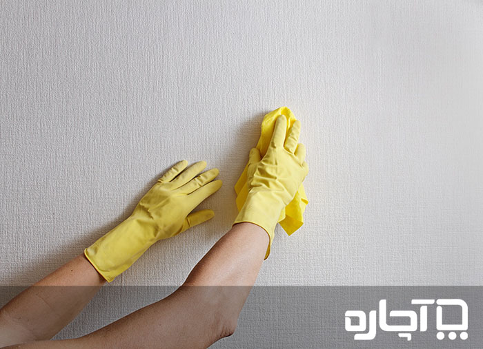 دستی زنانه با دستکش در حال تمیز کردن کاغذ دیواری